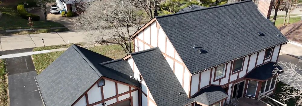 Aerial view of house with dark shingle roof.